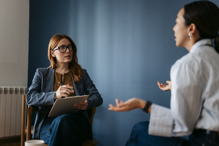 Psychologist taking notes while listening to young woman client talking during therapy session